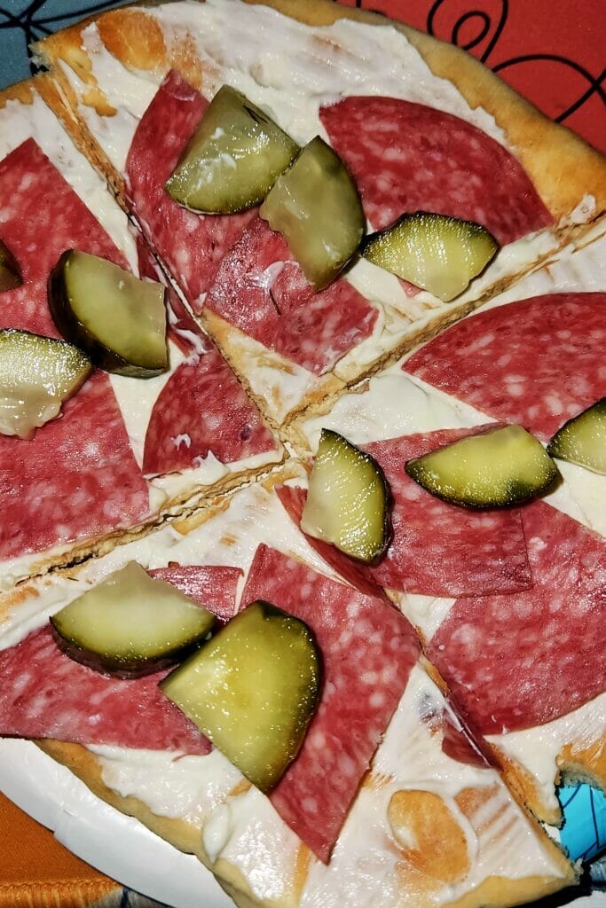 Naan flatbread cut into triangles and topped with whipped cream cheese, salami and dill pickle pieces.