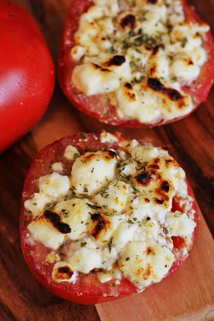 Two tomatoes sliced in half, topped with feta and mozzarella cheese, Italian seasoning and Italian dressing. The cheese is lightly browned on top from broiling.