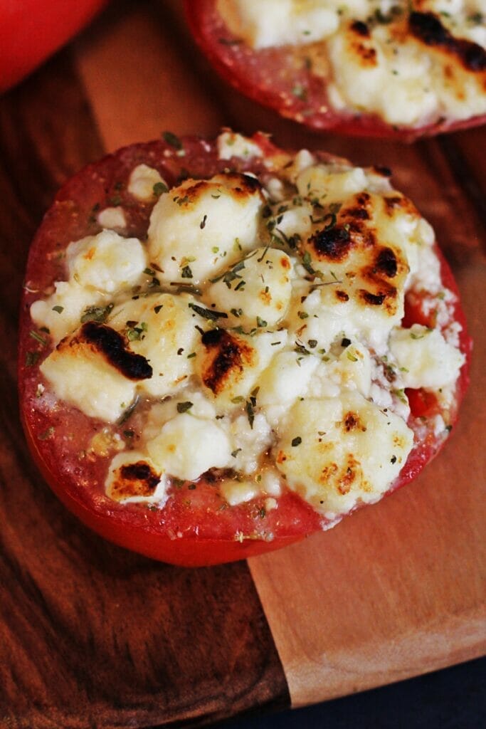 Two tomatoes sliced in half, topped with feta and mozzarella cheese, Italian seasoning and Italian dressing. The cheese is lightly browned on top from broiling.